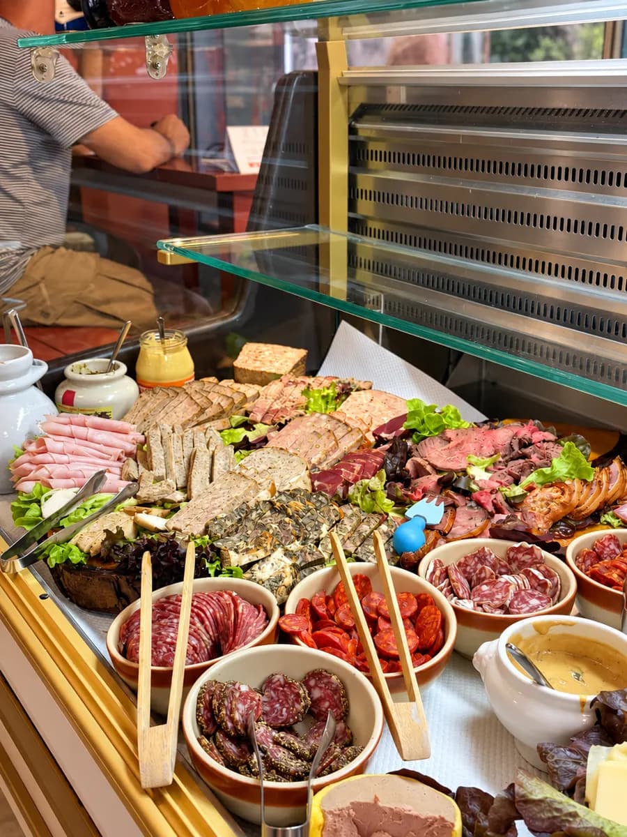 Vitrine mit Charcuterie: Schinken, Pasteten, Terrinen und Schalen mit Salami.