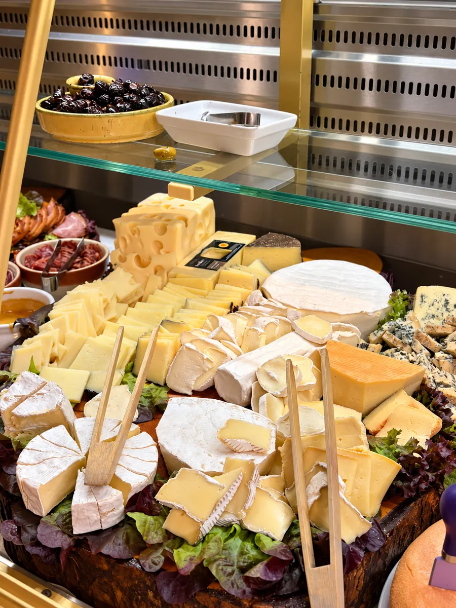 Käseauswahl in der Vitrine: Emmentaler, Camembert, Ziegenkäse und Blauschimmelkäse auf Salatblättern.